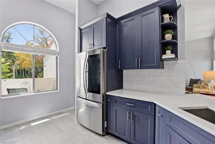 Kitchen featuring navy cabinetry, white countertops, stainless steel appliances, a white subway tile backsplash, and a large arched window