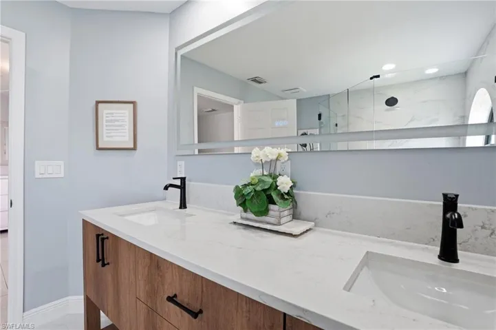 Dual vanity with wood-finish cabinetry and white countertops, featuring integrated sinks and matte black faucets