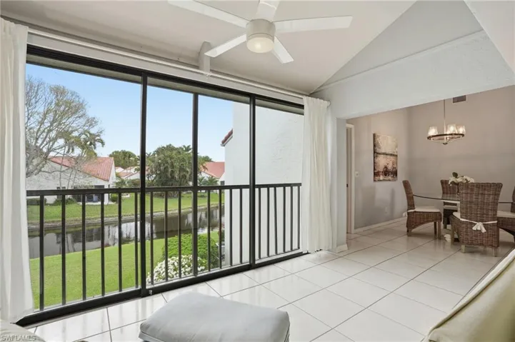 Screened balcony with waterway views, featuring white tile flooring, a ceiling fan, and an open concept dining area with a chandelier