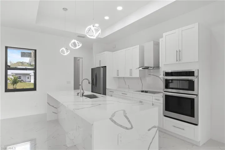 Kitchen with a sink, wall chimney range hood, appliances with stainless steel finishes, a raised ceiling, and a large island with sink
