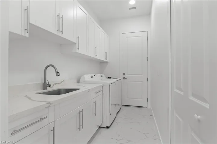 Washroom featuring marble finish floor, cabinet space, washing machine and dryer, a sink, and baseboards