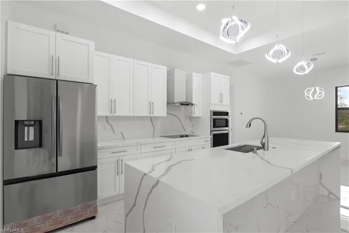 Kitchen featuring wall chimney exhaust hood, marble finish floor, stainless steel appliances, white cabinetry, and a sink