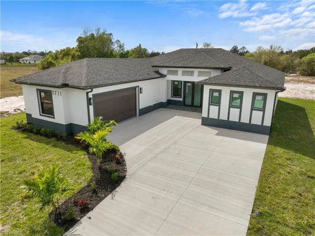 View of front of house featuring a garage, a shingled roof, a front lawn, and stucco siding