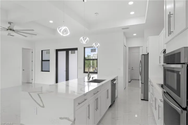 Kitchen featuring marble finish floor, a spacious island, stainless steel appliances, white cabinetry, and a sink