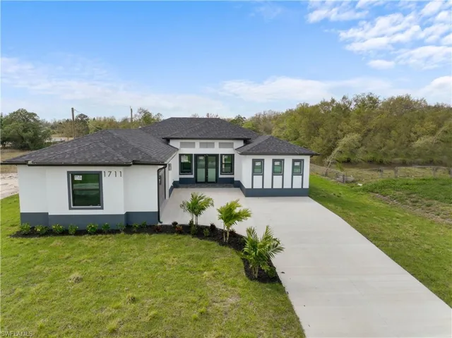 View of front of home featuring driveway, roof with shingles, a front lawn, and stucco siding