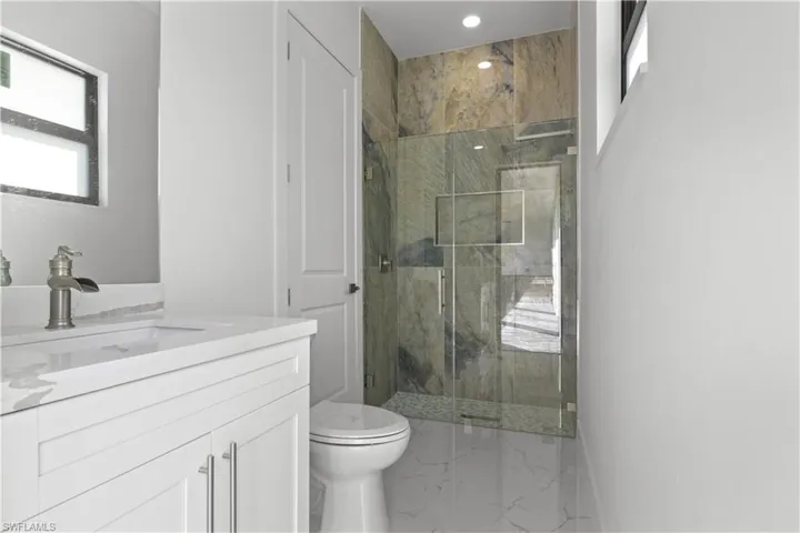 Full bath with a marble finish shower, toilet, marble finish floor, vanity, and recessed lighting