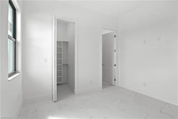 Unfurnished bedroom with marble finish floor, baseboards, a walk in closet, and a closet