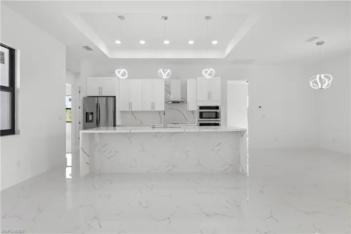 Kitchen featuring wall chimney range hood, stainless steel refrigerator with ice dispenser, a raised ceiling, and white cabinets