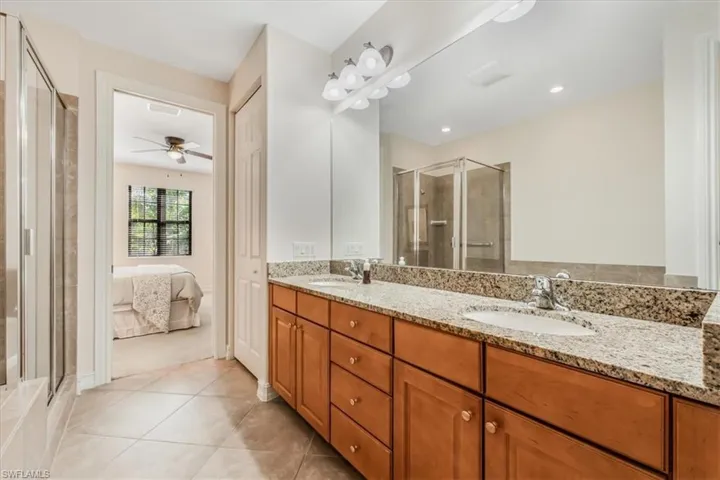 Ensuite bathroom featuring double vanity, tile patterned floors, a shower stall, and ceiling fan