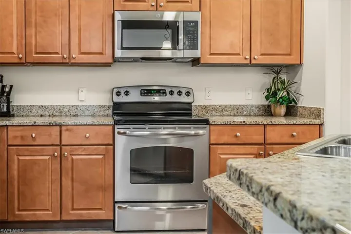 Kitchen featuring appliances with stainless steel finishes, brown cabinetry, and light stone counters