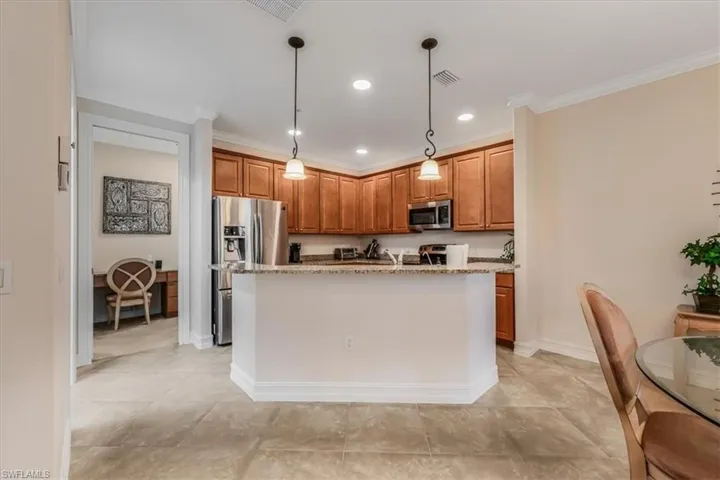 Kitchen with brown cabinets, stainless steel appliances, light stone countertops, crown molding, and a kitchen island with sink