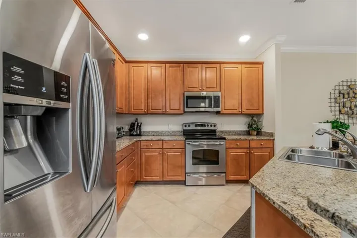 Kitchen with stainless steel appliances, ornamental molding, light tile patterned floors, brown cabinetry, and recessed lighting