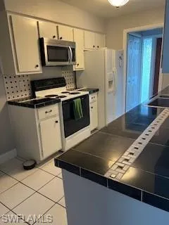 Kitchen featuring stove, white cabinetry, refrigerator, light tile patterned flooring, and tile counters
