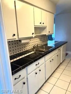Kitchen with tasteful backsplash, light tile patterned flooring, white cabinets, and tile counters