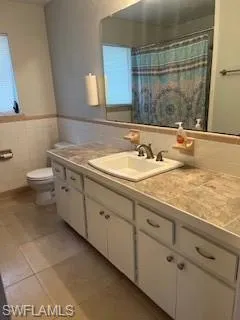 Full bathroom with vanity, tile walls, tile patterned floors, wainscoting, and a shower with curtain