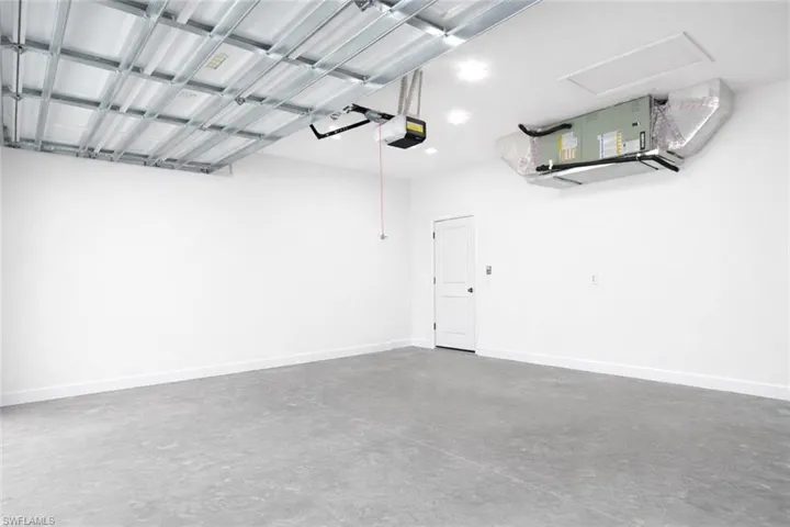 Spacious garage with a concrete floor, bright white walls, and a recessed panel door