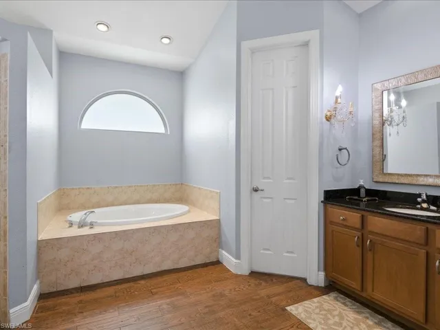 Bathroom with tiled tub, hardwood / wood-style flooring, and vanity