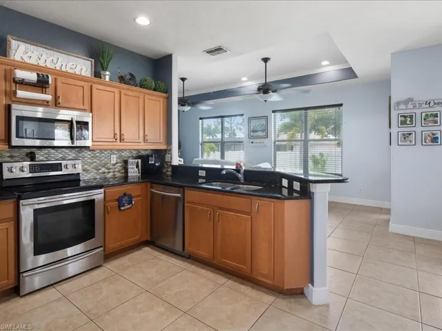 Kitchen featuring stainless steel appliances, a raised ceiling, dark quartzite counters, eat in kitchen peninsula, and ceiling fan