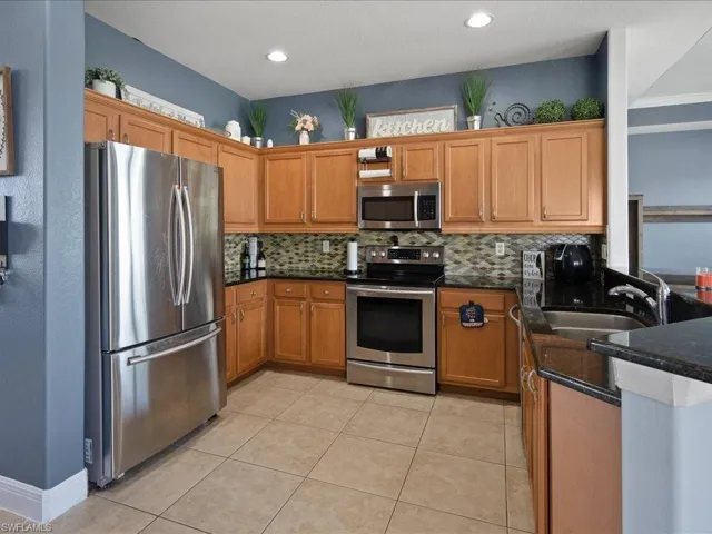 Kitchen featuring stainless steel appliances, decorative backsplash, sink, light tile floors, and dark quartzite counters