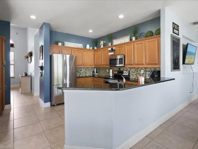 Kitchen with stainless steel appliances, tasteful backsplash, dark quartzite counters, kitchen peninsula, and  tile flooring