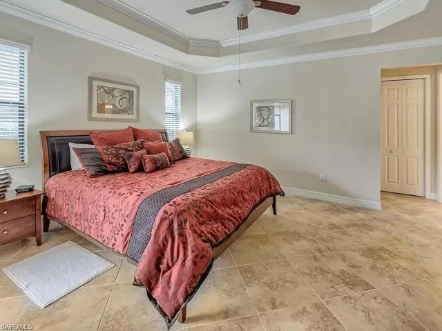 Bedroom with ceiling fan, crown molding, a tray ceiling, and light tile patterned floors