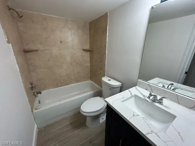 Full bathroom featuring vanity, hardwood / wood-style floors, tiled shower / bath combo, and toilet