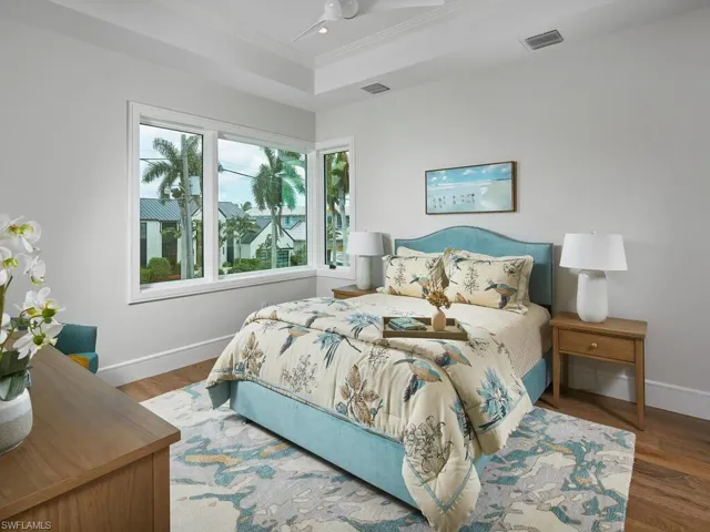 Bedroom with ceiling fan, a tray ceiling, and wood-type flooring