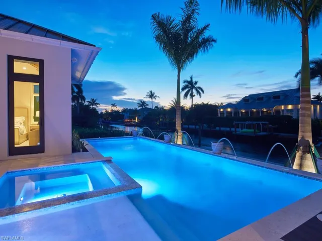 Pool at dusk featuring pool water feature and an in ground hot tub