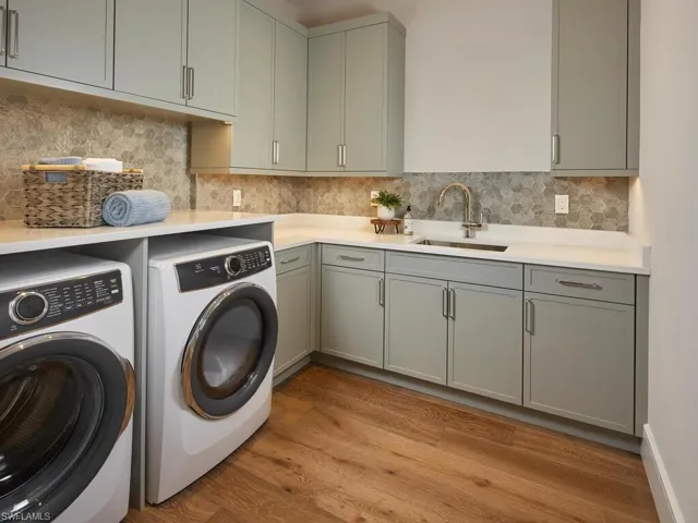 Clothes washing area with sink, cabinets, light wood-type flooring, and separate washer and dryer