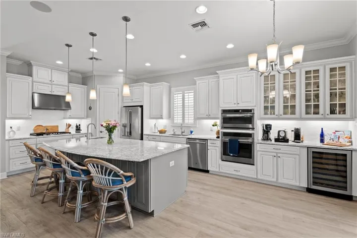 Spacious kitchen featuring white cabinetry, light-toned wood-finish flooring, a large island with granite countertops, stainless steel appliances, and a built-in wine refrigerator