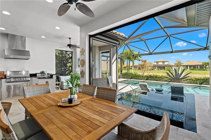 Expansive outdoor living area featuring an integrated kitchen with stainless steel appliances, a screened lanai, and an in-ground swimming pool