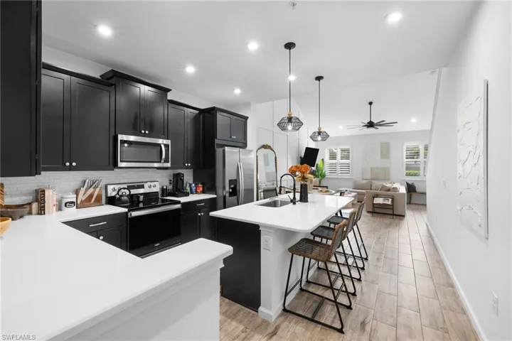 Kitchen with dark cabinets, stainless steel appliances, decorative light fixtures, a kitchen island with sink, and open floor plan