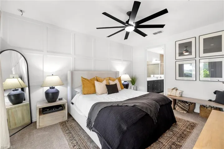 Carpeted bedroom featuring a decorative wall, a ceiling fan, and connected bathroom