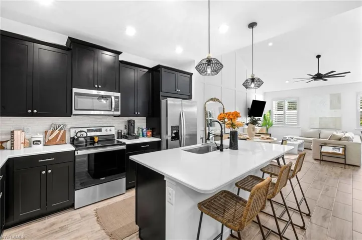 Kitchen featuring dark cabinets, stainless steel appliances, open floor plan, light stone countertops, and lofted ceiling