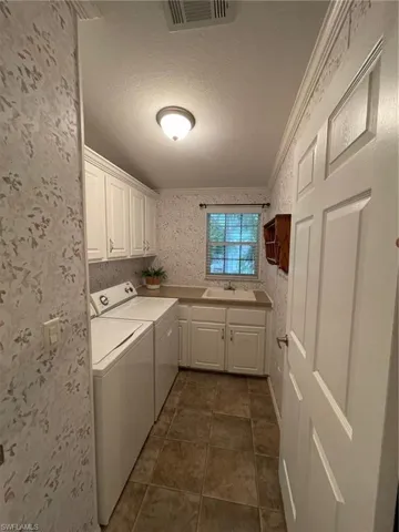 Laundry room with cabinets, dark tile floors, washer and clothes dryer, ornamental molding, and sink