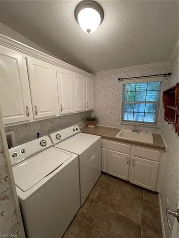 Laundry area featuring dark tile flooring, ornamental molding, washing machine and dryer, sink, and a textured ceiling