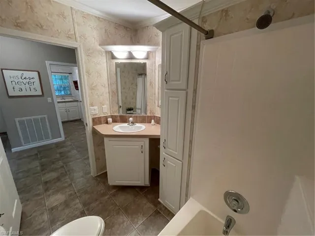 Full bathroom with vanity with extensive cabinet space, toilet, tile floors, shower / bath combination with curtain, and ornamental molding