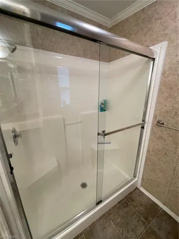 Bathroom featuring a shower with door, tile flooring, and ornamental molding