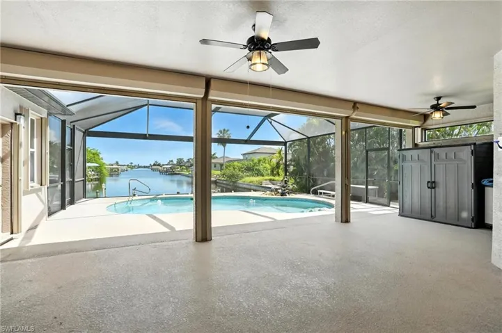 Outdoor pool with a ceiling fan, a patio, a water view, and glass enclosure