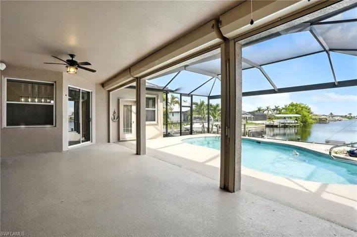 Swimming pool featuring a water view, a ceiling fan, a patio, and glass enclosure