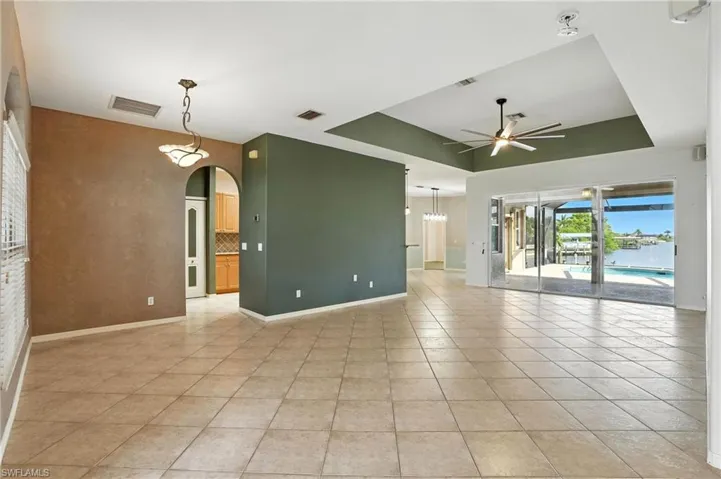 Spare room with a raised ceiling, light tile patterned floors, ceiling fan, and arched walkways