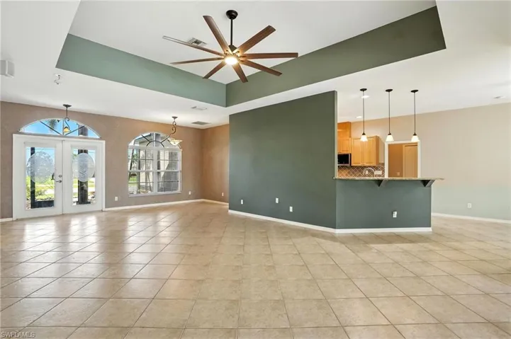 Unfurnished living room with light tile patterned flooring, ceiling fan, french doors, and a tray ceiling