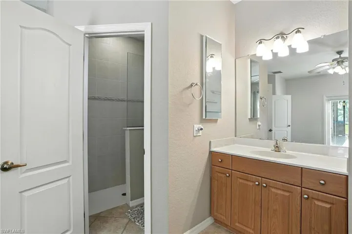 Full bathroom with a textured wall, vanity, a tile shower, tile patterned flooring, and a ceiling fan