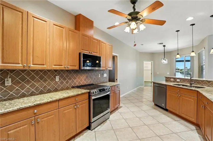 Kitchen with tasteful backsplash, appliances with stainless steel finishes, ceiling fan, light tile patterned flooring, and light stone countertops