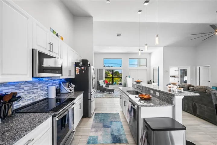Kitchen featuring a center island with sink, sink, decorative light fixtures, white cabinetry, and stainless steel appliances