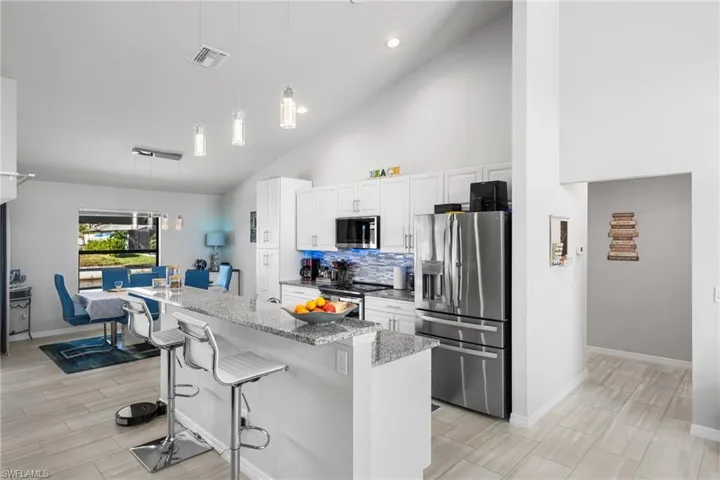 Kitchen with light stone countertops, stainless steel appliances, a kitchen breakfast bar, pendant lighting, and white cabinets