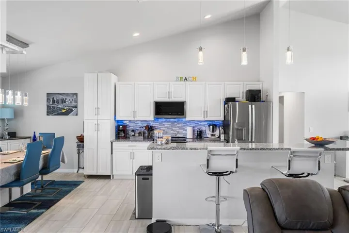 Kitchen with backsplash, light stone counters, stainless steel appliances, decorative light fixtures, and white cabinetry