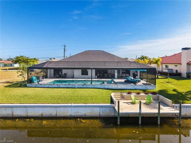Back of property with a lawn, a lanai, and a water view