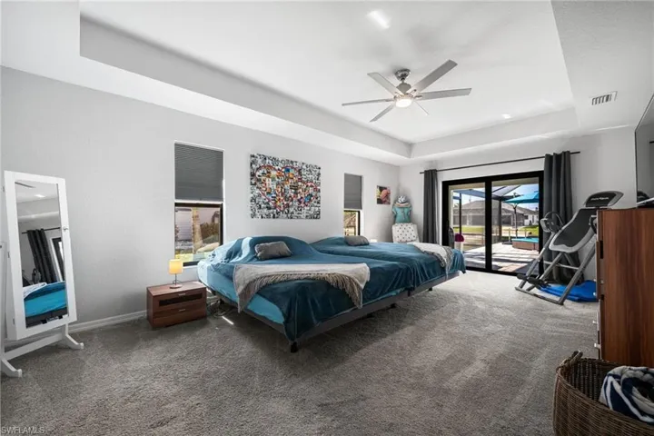 Bedroom with access to exterior, carpet flooring, a tray ceiling, and ceiling fan