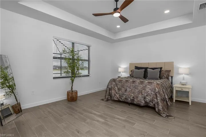 Primary bedroom with tray ceiling, sliding doors, and water view. (photos from staged home in community)
